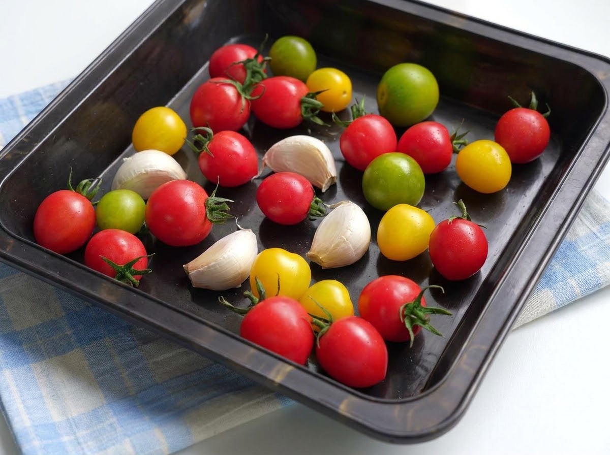 Una teglia da forno riempita con pomodorini colorati e spicchi daglio conditi con olio doliva e spezie.