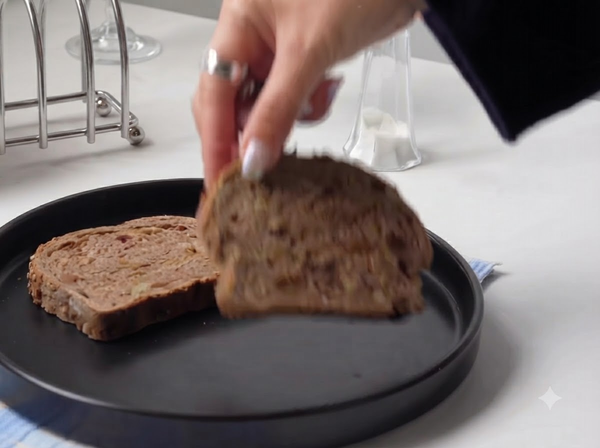 Una mano che posiziona una fetta spessa di pane rustico su un piatto rotondo nero.