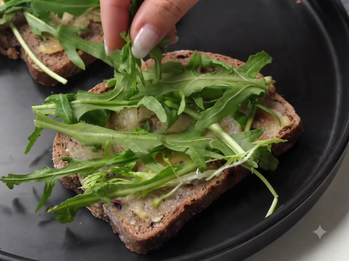 Una persona che dispone fette di prosciutto crudo sopra la rucola verde fresca su una fetta di pane.