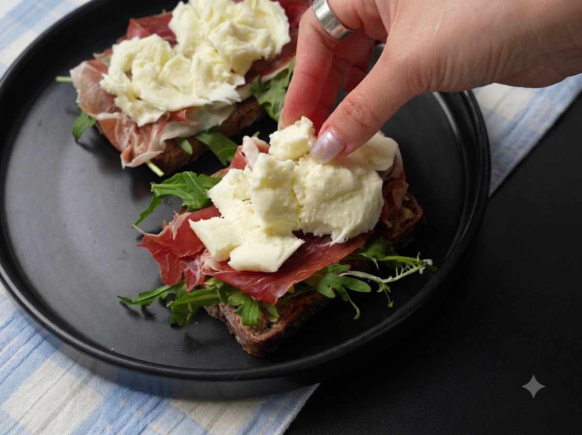 Pezzi freschi di mozzarella strappata posizionati sopra lo strato di prosciutto sul panino.