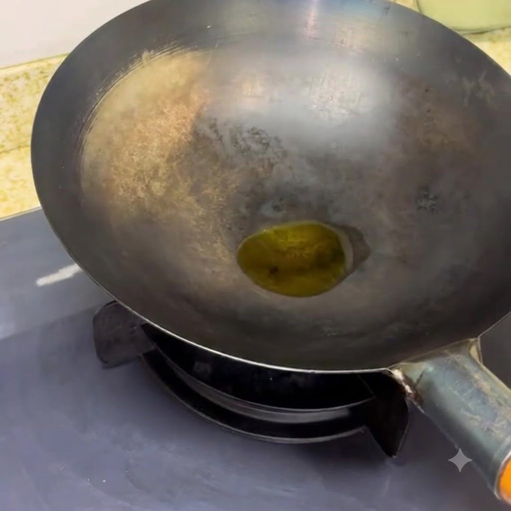Un wok nero appoggiato su un fornello con una piccola pozza di olio che si scalda allinterno.