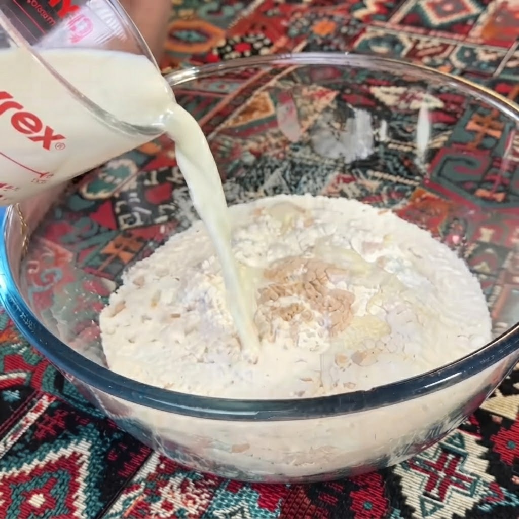 Latte versato da un bicchiere misuratore trasparente in una ciotola di farina e lievito.