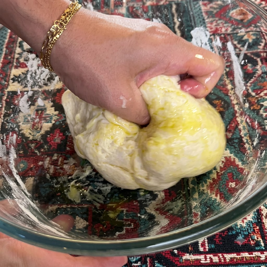 Una mano che impasta e piega energicamente limpasto mescolato con olio doliva allinterno di una ciotola di vetro.