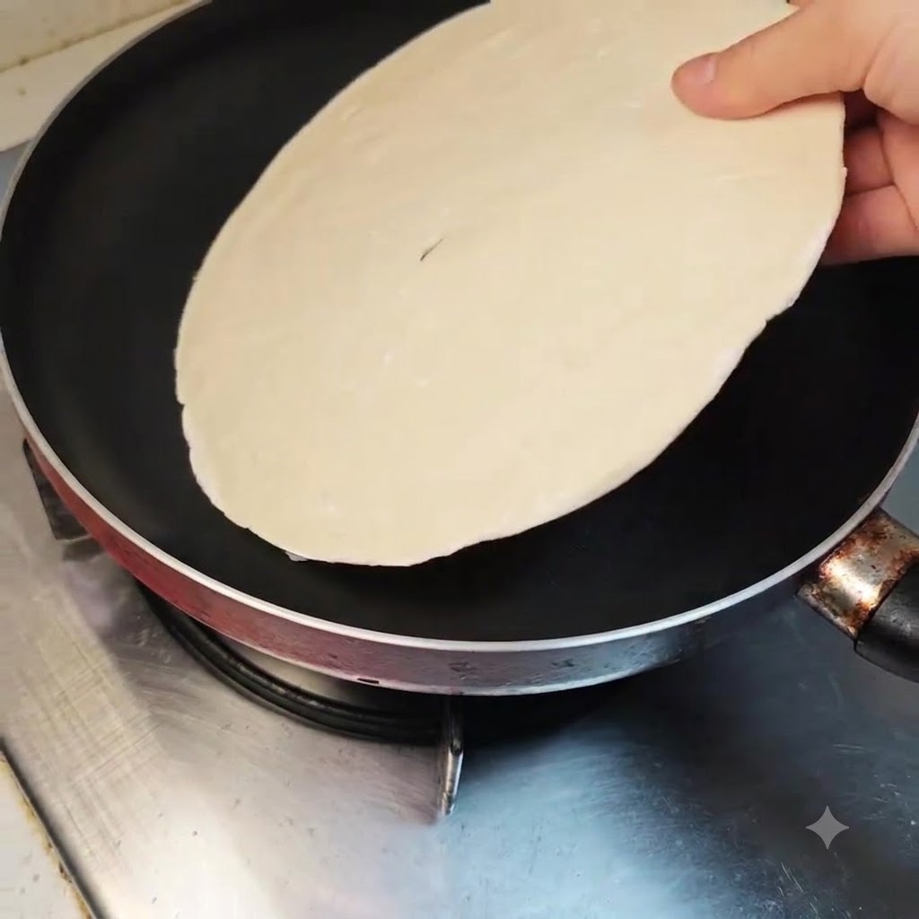 Un pancake ai cipollotti steso piatto allinterno di una padella antiaderente pulita su un fornello spento.