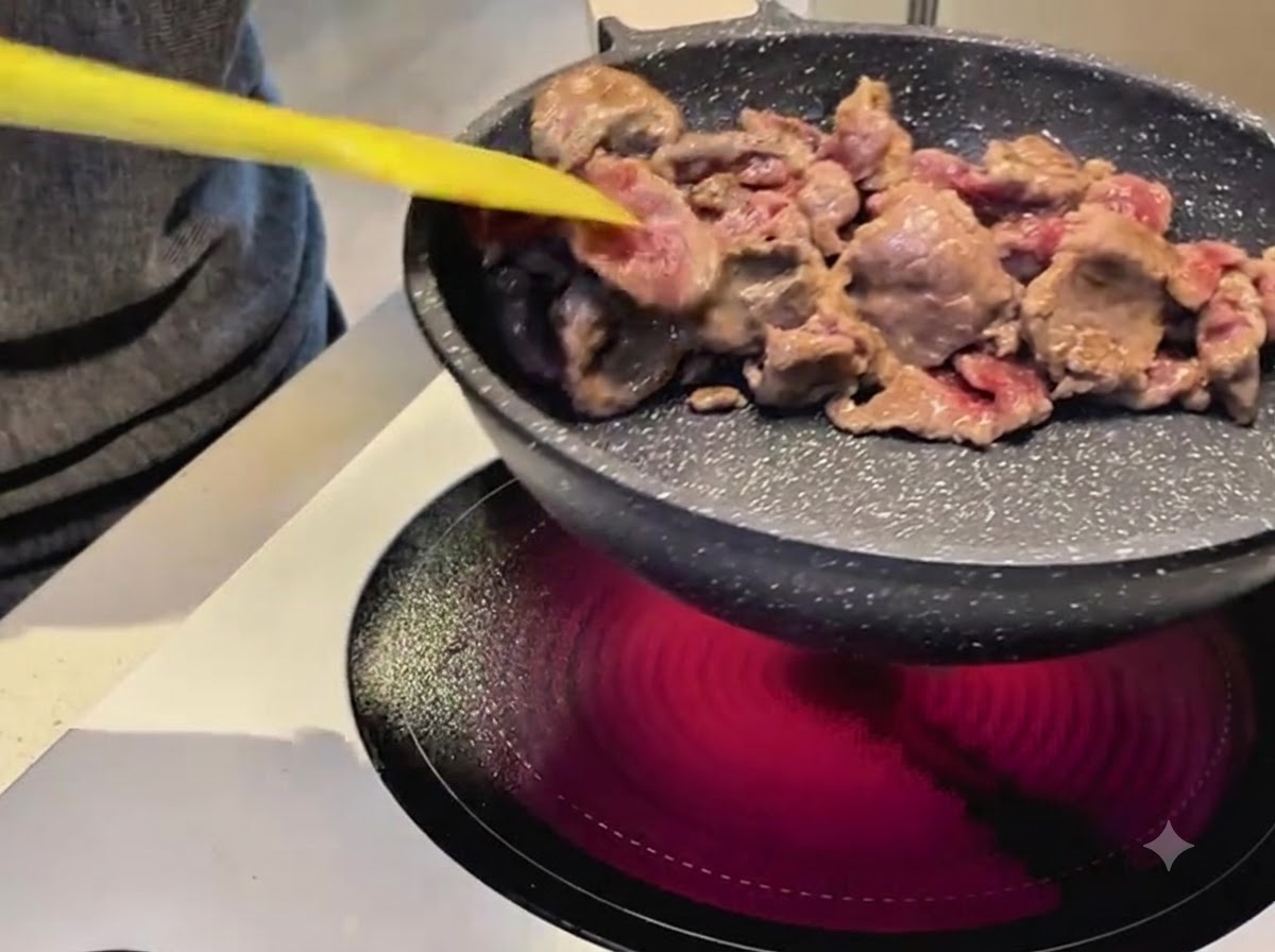 Uso di una spatola gialla per saltare fettine di manzo in una padella antiaderente su un fornello elettrico.