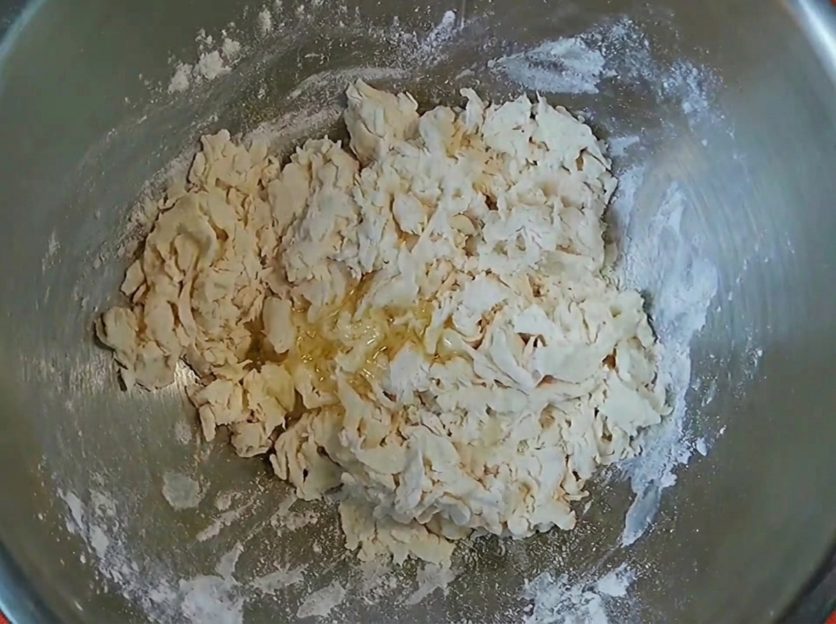 Fiocchi di impasto con un filo di olio da cucina allinterno di una ciotola di miscelazione in metallo.