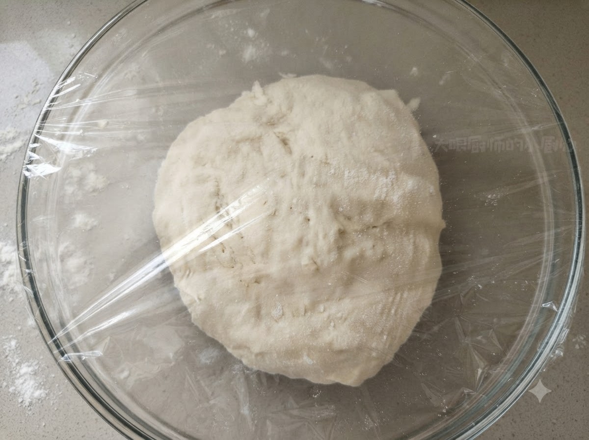 Una palla di impasto liscia allinterno di una ciotola di vetro trasparente coperta saldamente con pellicola trasparente di plastica.