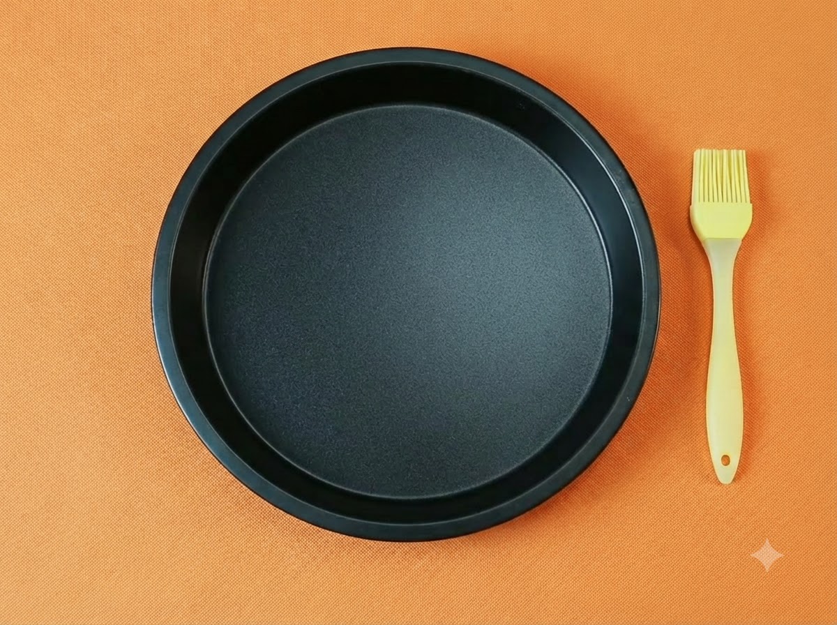 Una teglia per pizza rotonda nera vuota abbinata a un pennello da cucina in silicone giallo su sfondo arancione.