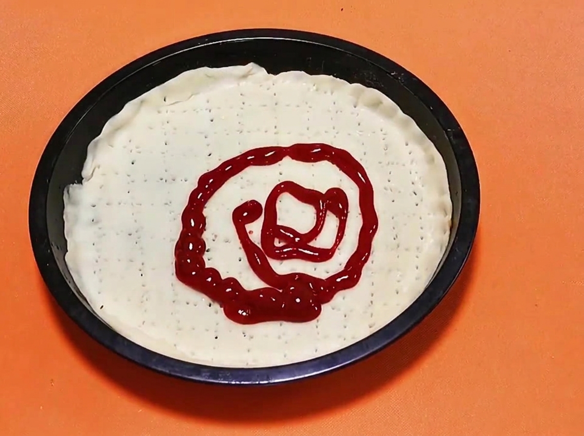Un motivo a spirale di salsa di pomodoro rosso vivo spremuta al centro di una base di pasta per pizza cruda.