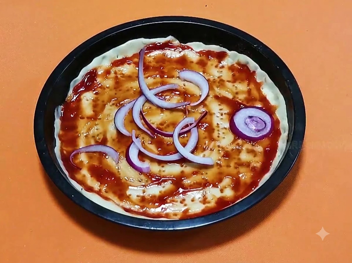Anelli di cipolla rossa affettati disposti su una base di pasta per pizza condita con salsa di pomodoro allinterno di una teglia rotonda nera.