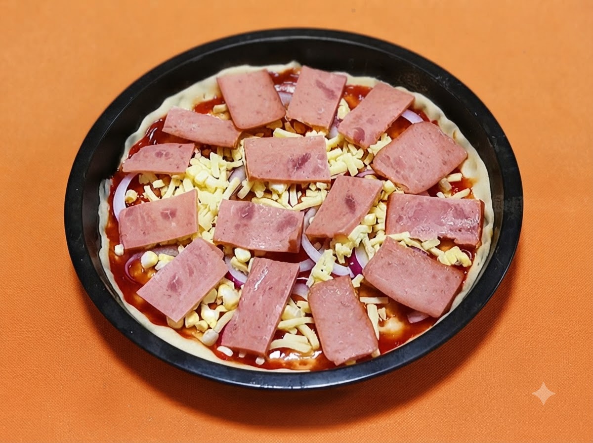Fette rettangolari di prosciutto rosa disposte sistematicamente su una base per pizza guarnita con formaggio e cipolle.