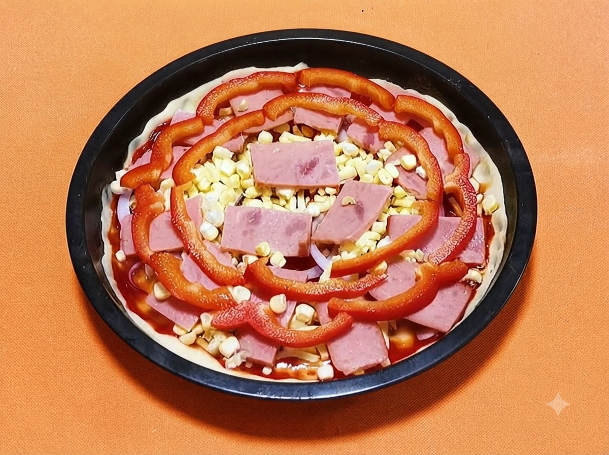 Crosta di pizza in una teglia nera guarnita con salsa, prosciutto, chicchi di mais giallo e fette di peperone rosso.