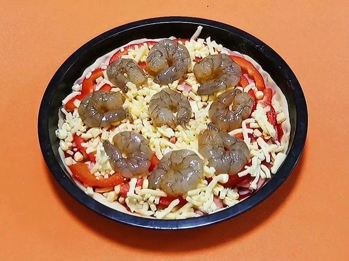 Gamberi crudi marinati disposti in cerchio sopra una pizza con formaggio, peperoni e prosciutto.
