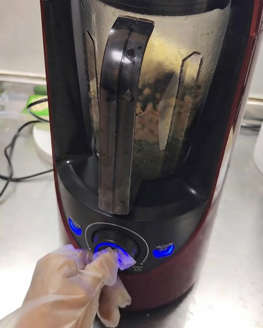 Un frullatore in funzione con gli ingredienti che si mescolano allinterno mentre una mano gira la manopola.