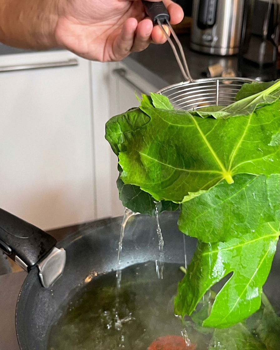 Un colino che solleva foglie verdi appena sbollentate da una pentola di acqua bollente.