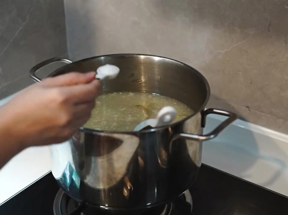 Aggiunta di un cucchiaio di sale a un brodo bianco latte e denso in una pentola di acciaio inossidabile.