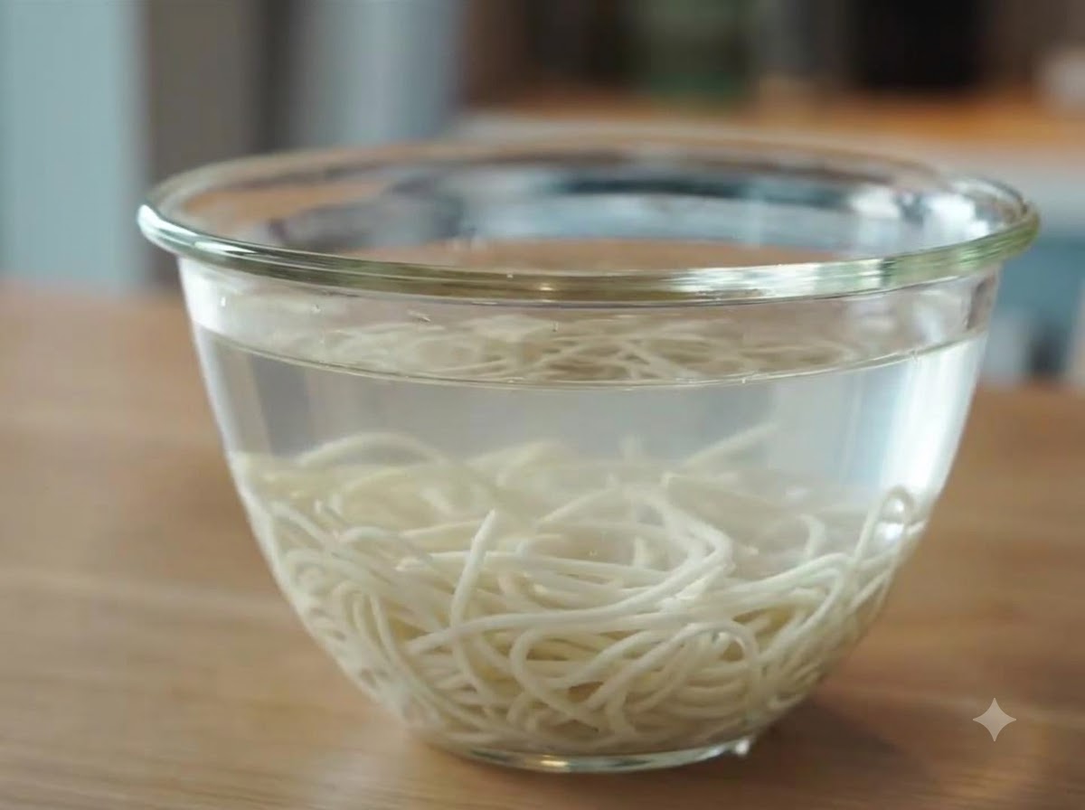 Noodles di ramen appena cotti immersi a raffreddare in una ciotola di vetro piena di acqua fredda.