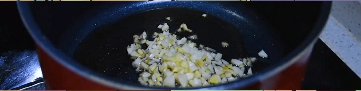 Zenzero e aglio tritati che sfrigolano in una pentola scura con olio di sesamo caldo.