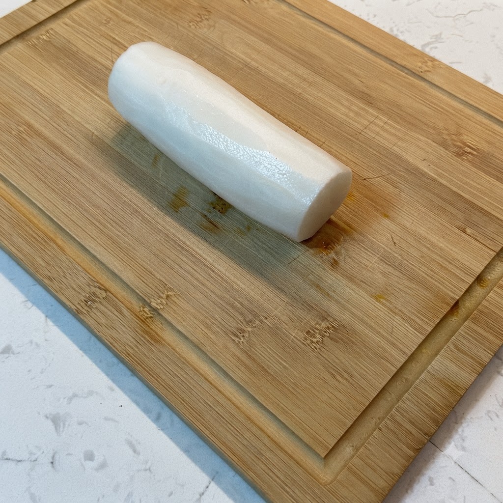Un ravanello bianco daikon tagliato a strisce sottili su un tagliere di legno.