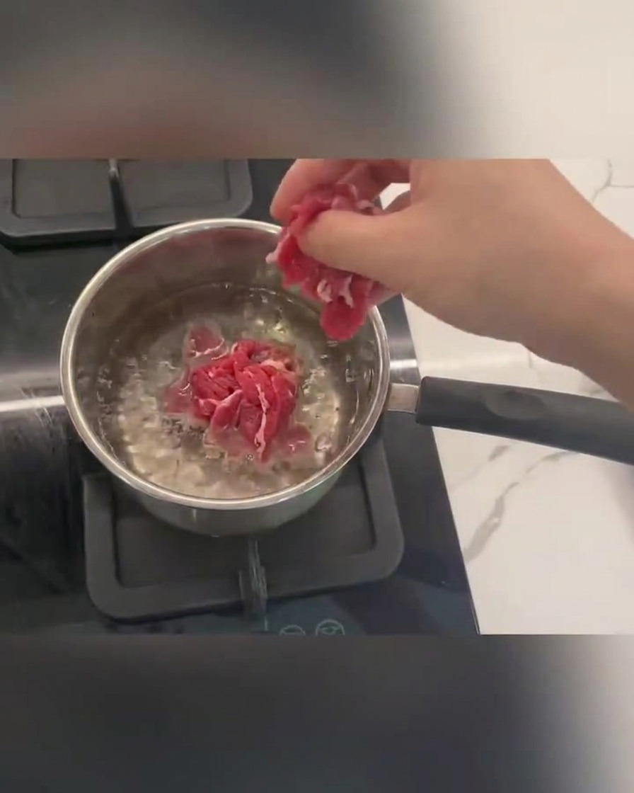 Fettine di manzo in cottura in acqua bollente con schiuma in superficie.