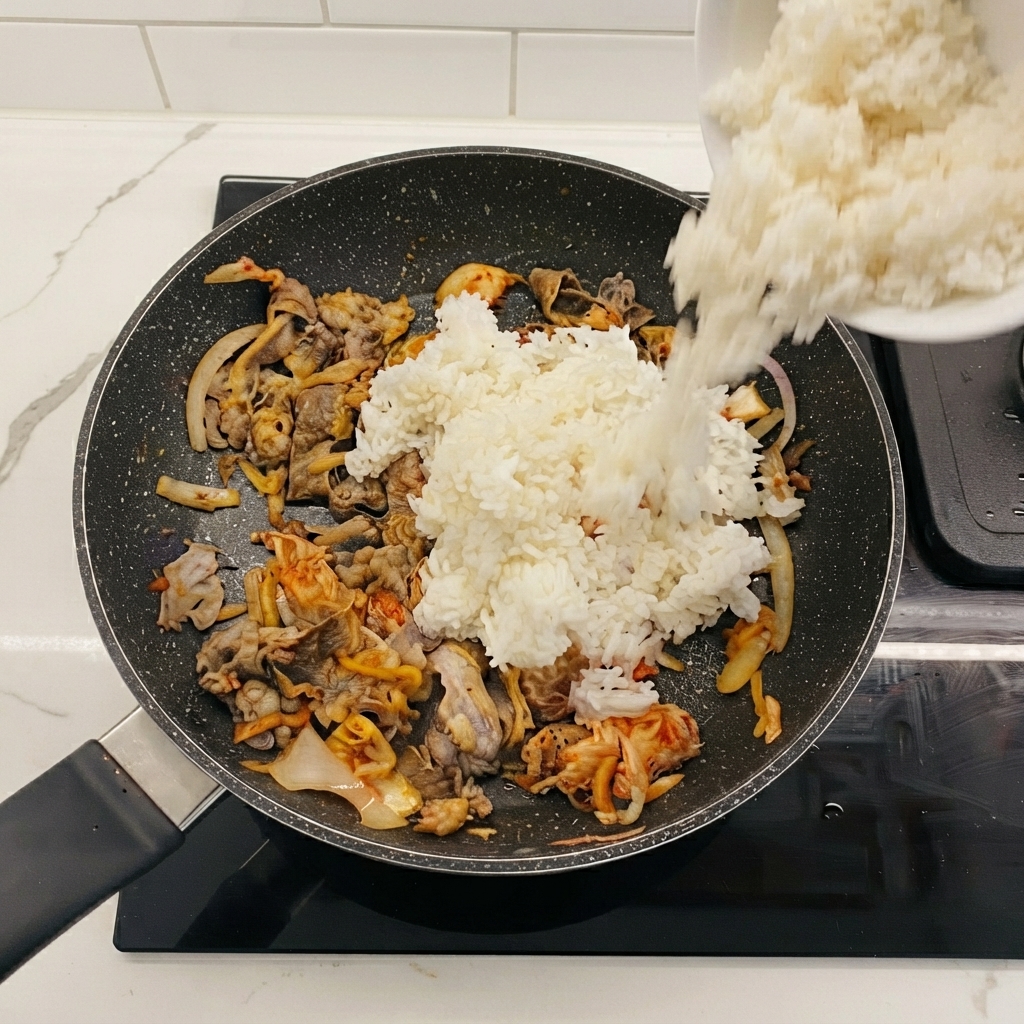 Riso bianco versato da una ciotola nella padella con manzo e kimchi.