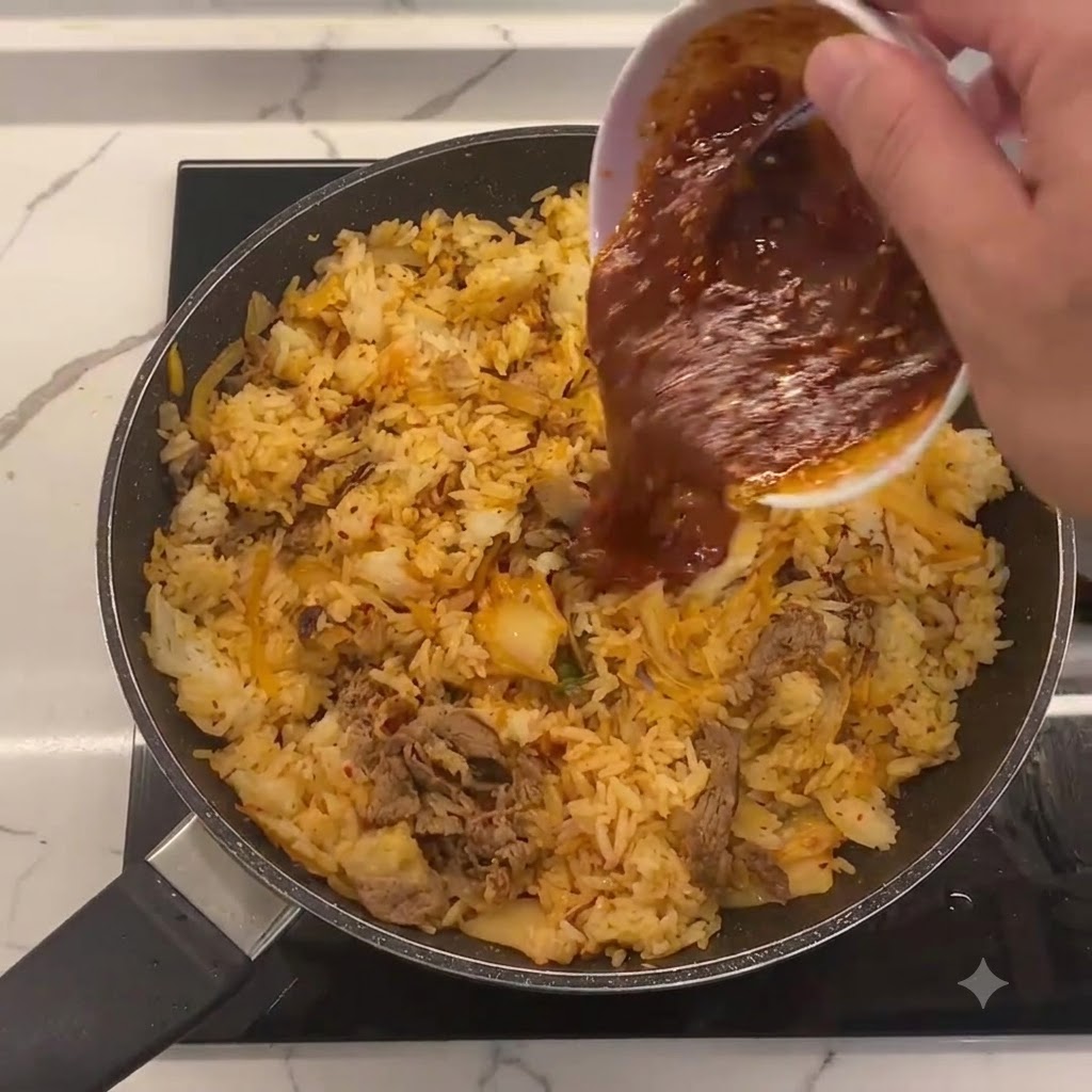 Salsa speciale versata da una ciotolina bianca al centro della padella con riso, kimchi e manzo.