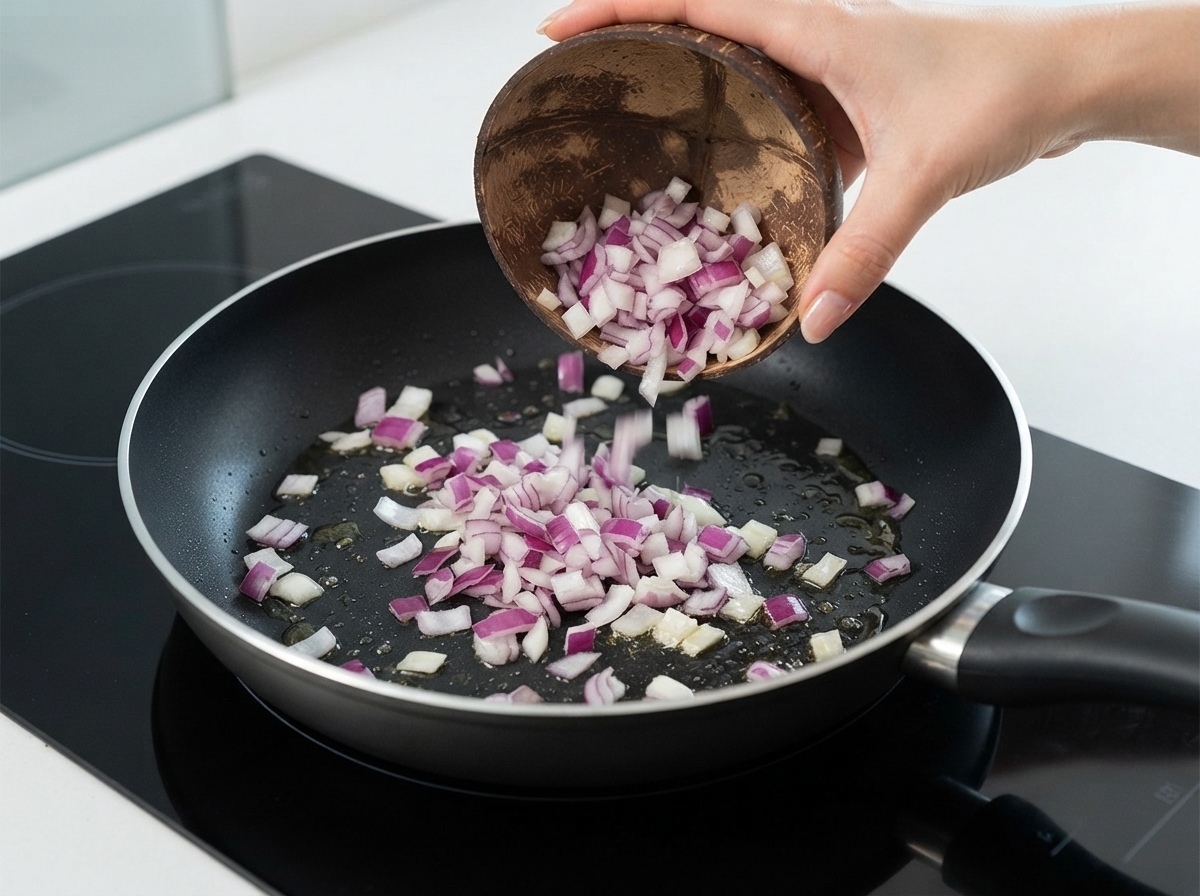 Cipolle rosse a dadini versate da una ciotola di cocco in una padella con olio.