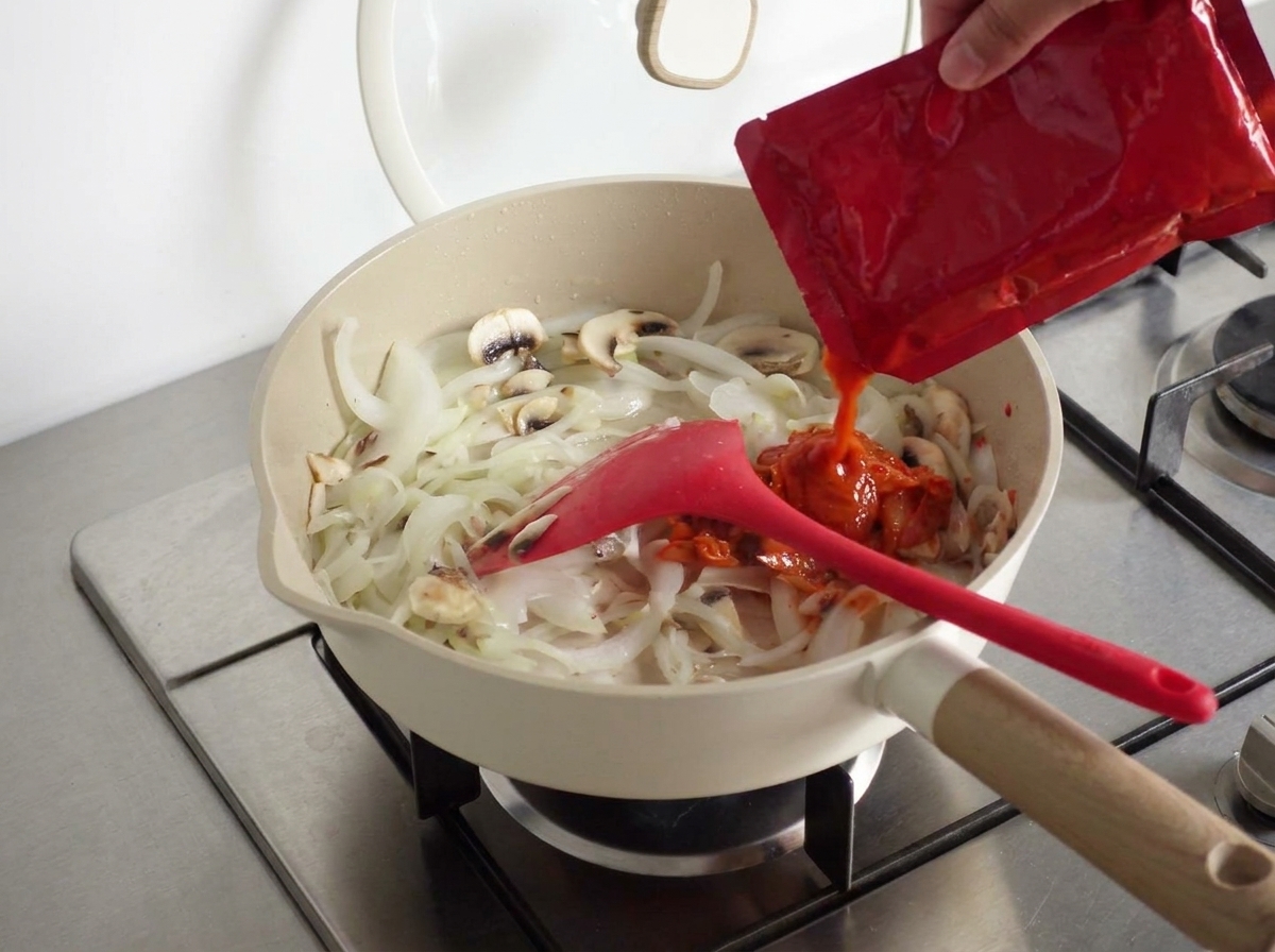 Un cucchiaio di pasta piccante coreana aggiunto al composto nella padella.