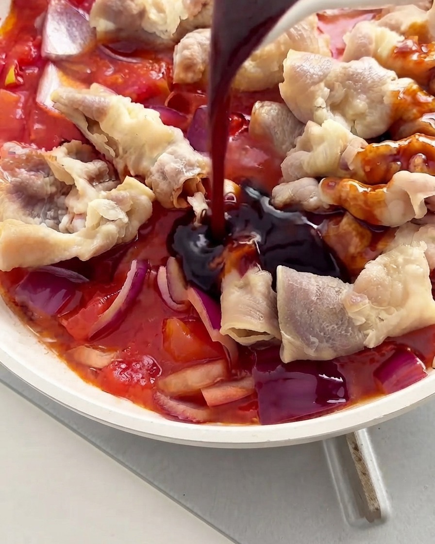 Salsa scura versata da un cucchiaio sugli involtini di manzo e sui pomodori allinterno di una padella bianca.