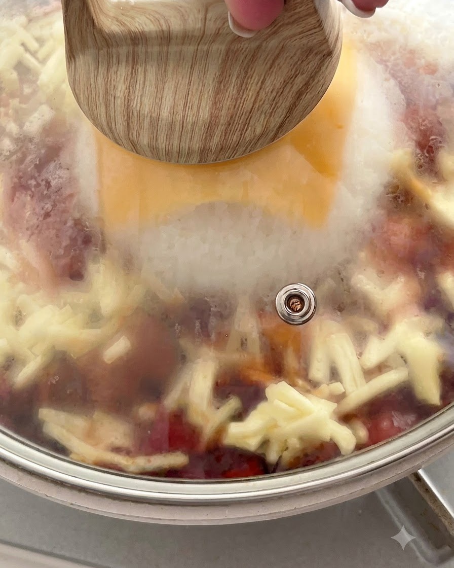 Una padella coperta con un coperchio di vetro che mostra il vapore intrappolato allinterno sopra il formaggio fondente e il riso.