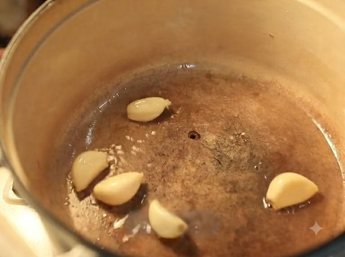 Spicchi daglio che friggono in olio caldo allinterno di una pentola in ghisa smaltata.