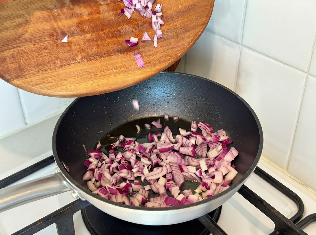 Cipolle rosse tritate versate da un tagliere in una padella calda con olio.