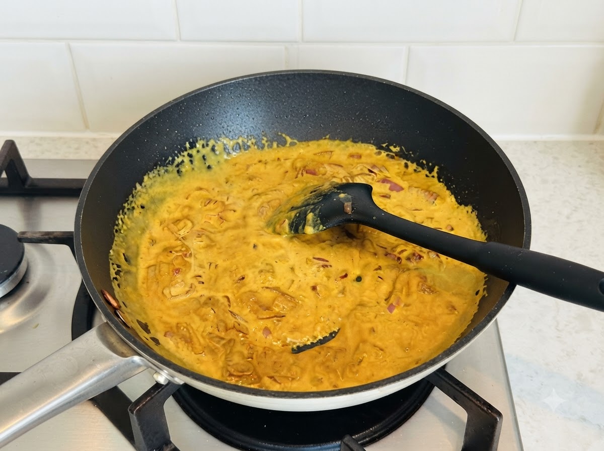 Ricca salsa al curry gialla mescolata in una padella scura con una spatola in silicone nero.
