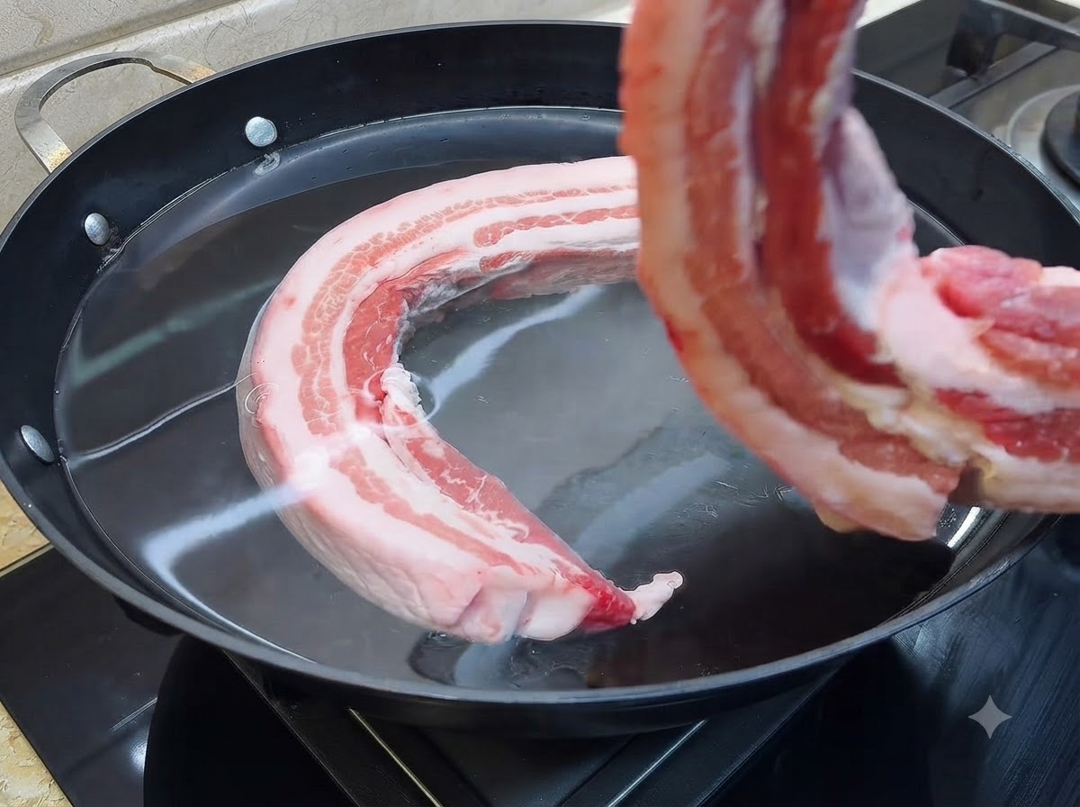 Un pezzo di pancia di maiale cruda immerso in una grande pentola piena di acqua fredda.