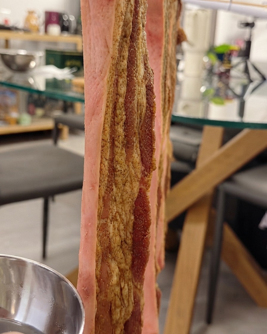 Pancetta di maiale appesa verticalmente su una rastrelliera mentre viene spennellata con lacqua speciale sulla pelle.