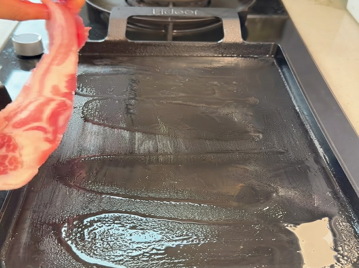 Una striscia di pancia di maiale cruda viene posizionata su una piastra teppanyaki calda.
