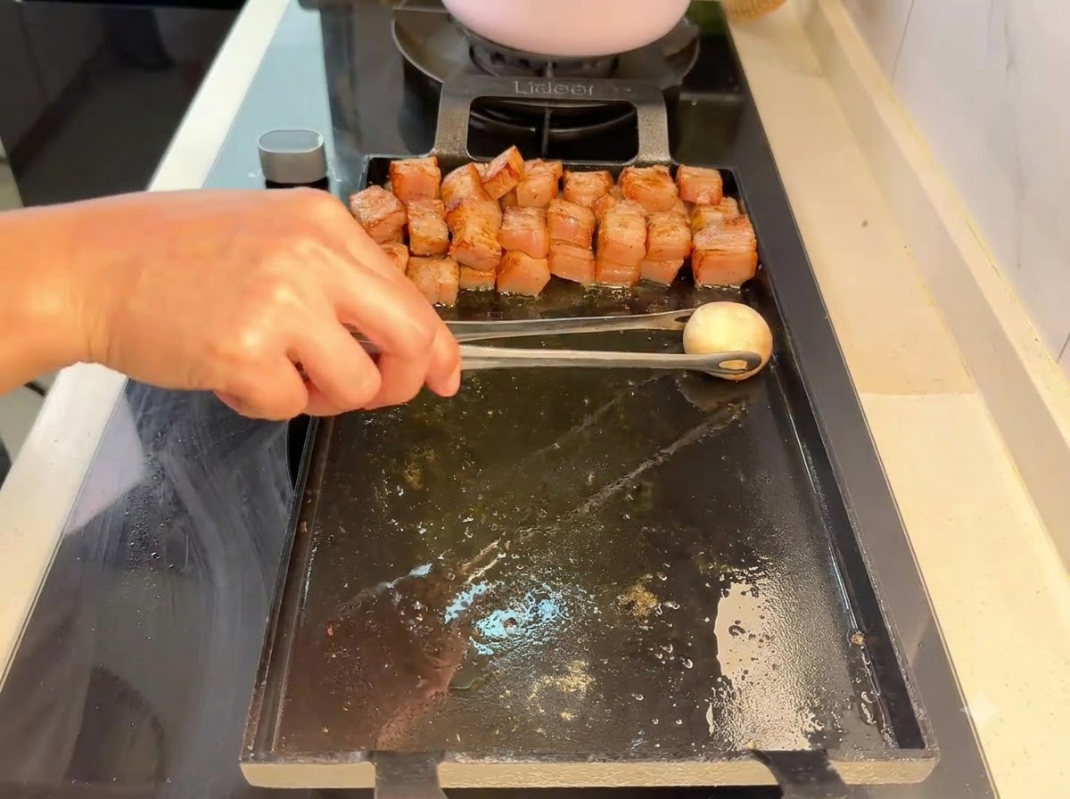 Un fungo champignon posizionato con le pinze sulla griglia accanto ai pezzi di maiale grigliati.