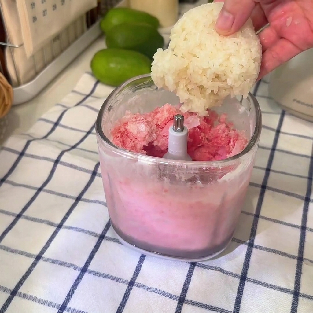 Una palla di riso glutinoso fatta cadere in una tazza trasparente del frullatore riempita con la miscela di granita di anguria rosa.