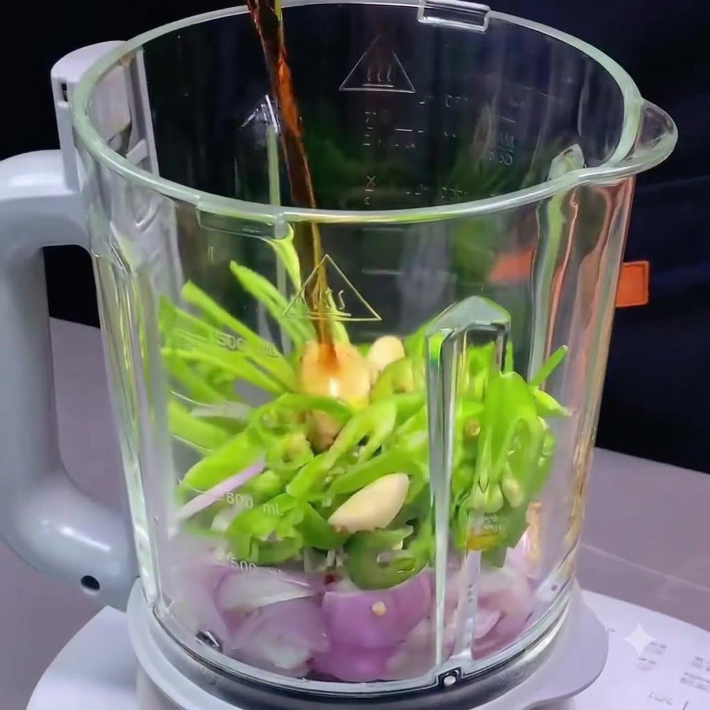 Condimenti liquidi versati nel contenitore del frullatore contenente peperoncini tritati, scalogno e aglio.