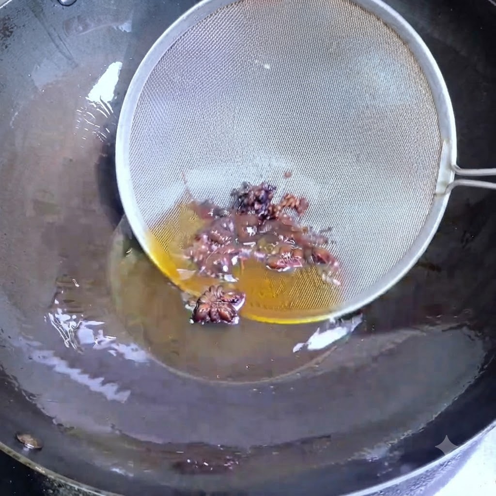 Un colino in filo metallico raccoglie lanice stellato scuro e i grani di pepe di Sichuan dallolio caldo in un wok.