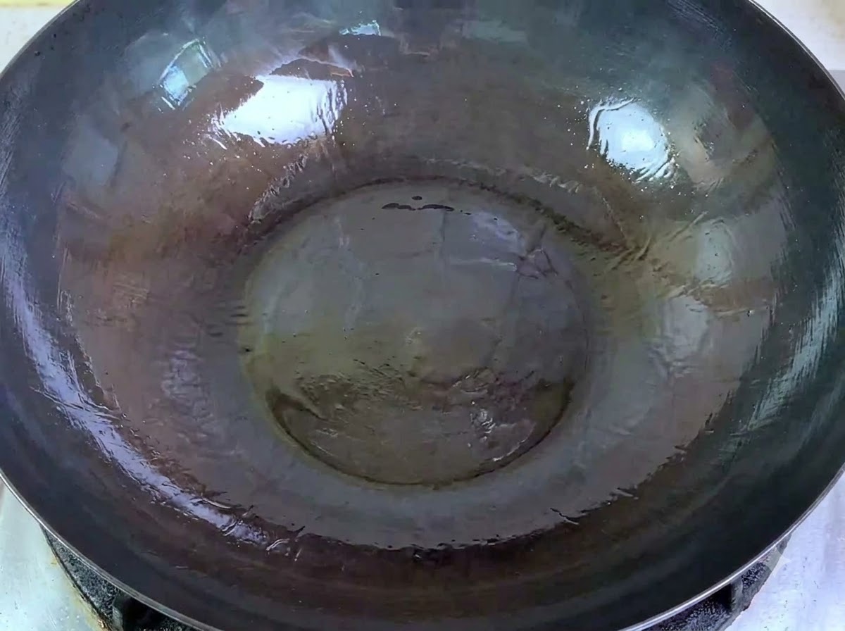 Maiale macinato crudo versato da una ciotola in un grande wok con olio ben caldo.