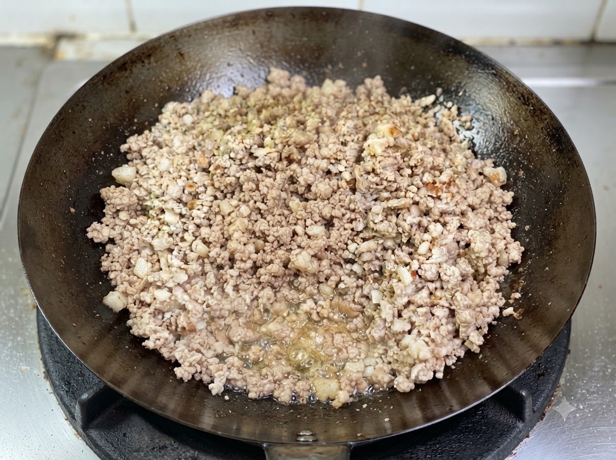 Maiale macinato che rosola in un wok, con lolio fuso che bolle chiaramente sul fondo.