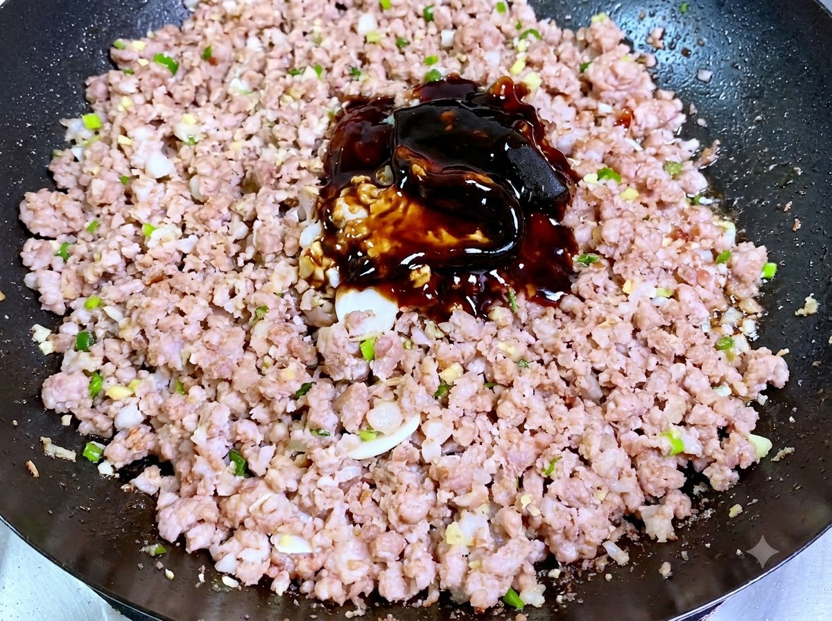 Un mucchietto di paste e salse scure di soia poste direttamente sopra la carne macinata cotta in un wok.