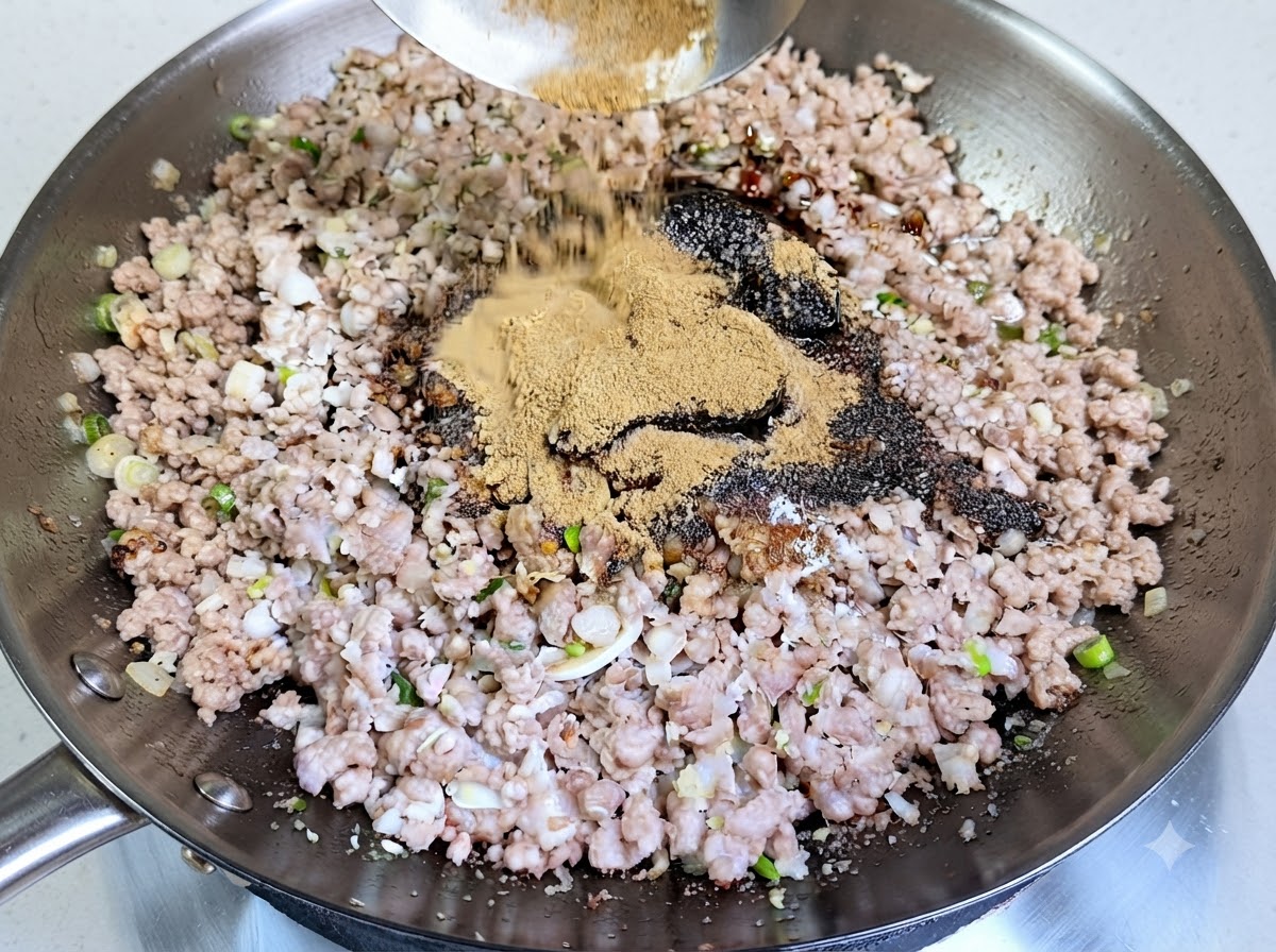 Unabbondante manciata di polvere di spezie sparsa con un mestolo sulla carne macinata condita in un wok.