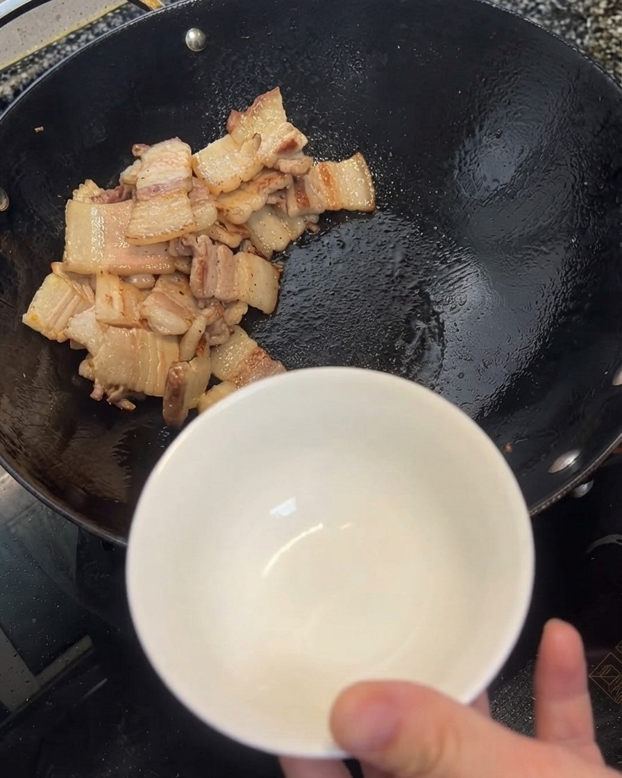Olio in eccesso che viene prelevato dal wok e versato in una ciotola bianca usando una spatola.