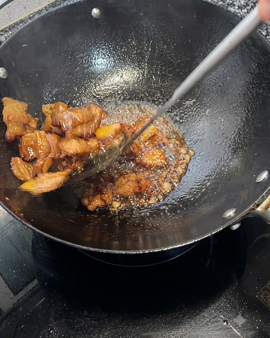 Pancetta di maiale che viene mossa rapidamente e rivestita di una salsa scura bollente in un wok.