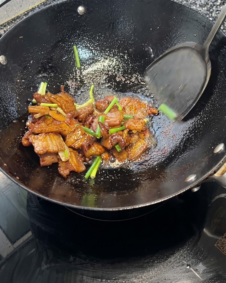 Una spatola che mescola insieme pancetta di maiale e cipollotti allinterno di un wok caldo.