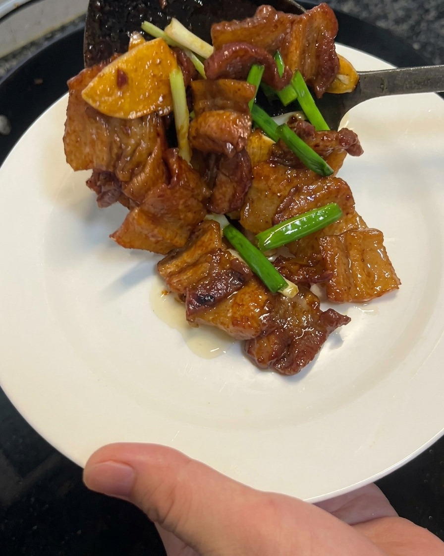 Pancetta di maiale cotta alla salsa di soia che viene sollevata da un wok con una spatola su un piatto bianco pulito.
