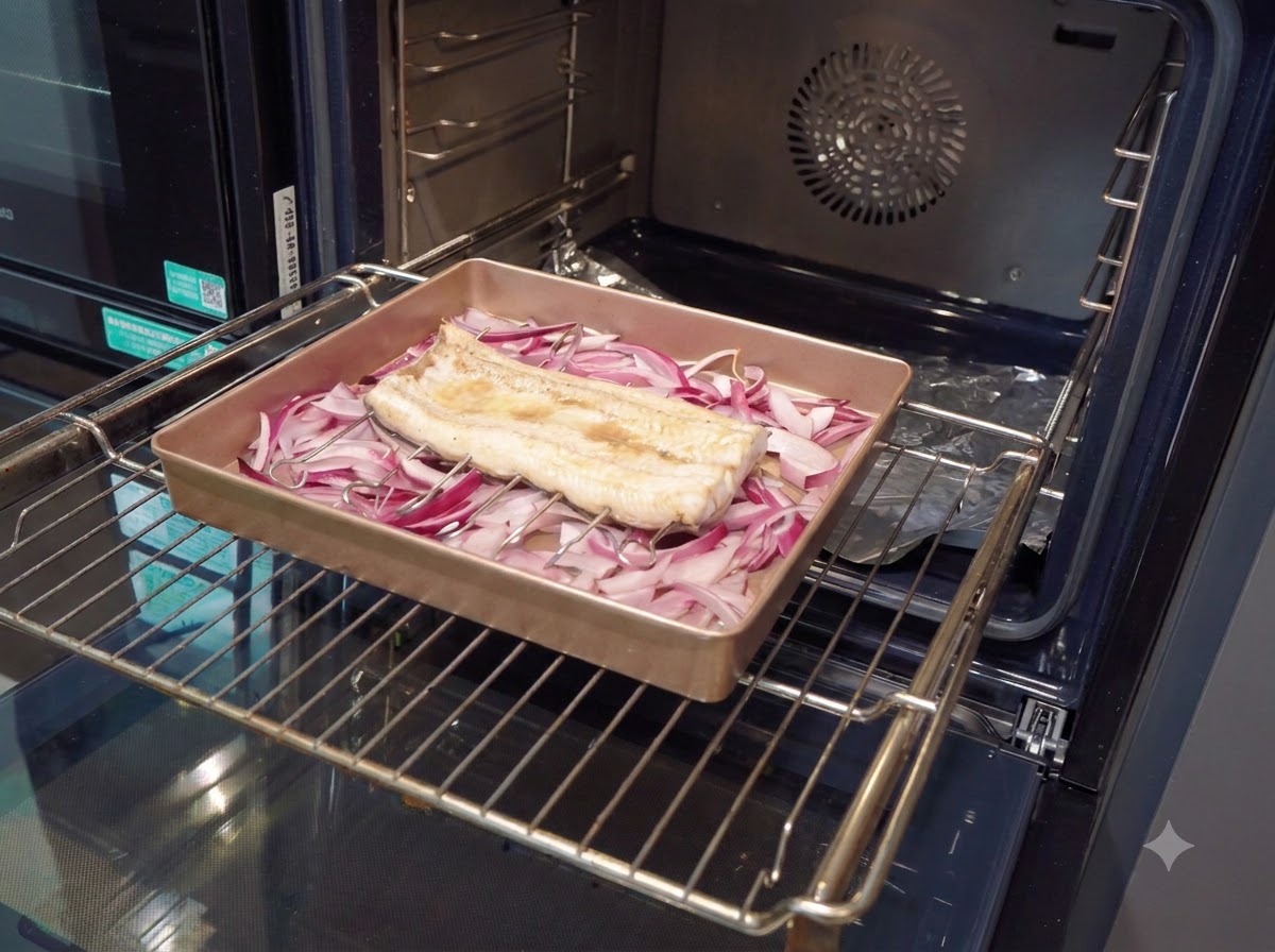 Un pennello da cucina che applica una salsa densa e marrone scuro su un filetto di anguilla parzialmente cotto allinterno di una teglia da forno.