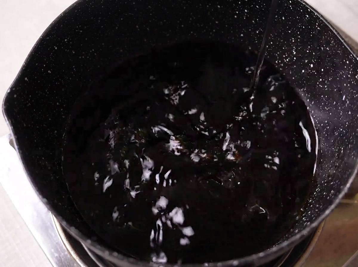 Salsa di soia, mirin, sake e zucchero bianco mescolati in una pentola scura su un piano cottura.
